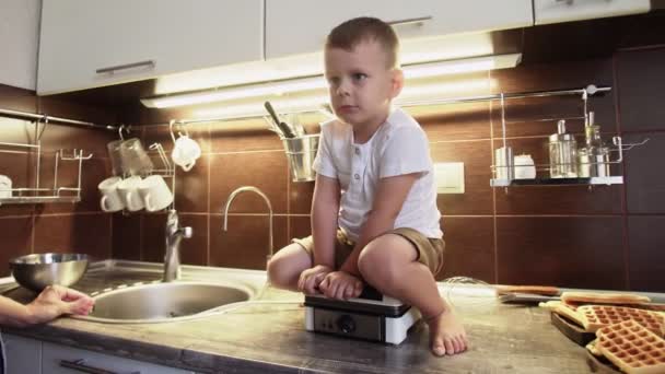 Kleiner Junge sitzt auf Waffelbäcker in Küche — Stockvideo