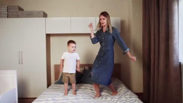 Η νεαρή μητέρα και το χαρούμενο αγοράκι της πηδούσαν στο μεγάλο κρεβάτι στην κρεβατοκάμαρα. — Αρχείο Βίντεο