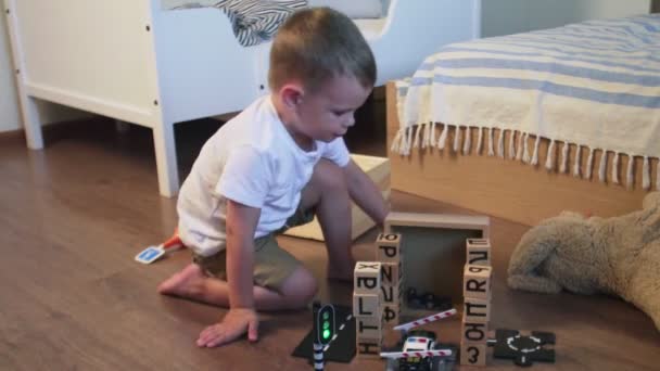 Menino se senta no chão e brinca com carros em casa — Vídeo de Stock