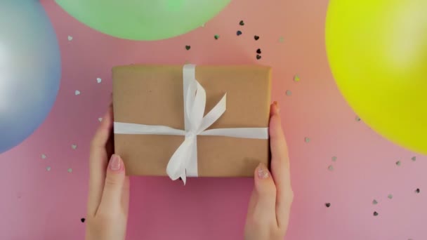 Žena putts vánoční dárek box zabalený v řemeslné papíru na růžovém stole — Stock video