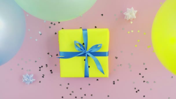 Woman takes Christmas birthday gift box wrapped in yellow paper with blue bow on pink table — Stock Video