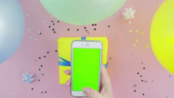 Visão superior da mulher usa telefone com tela verde com caixa de presente amarelo no backgound rosa — Vídeo de Stock