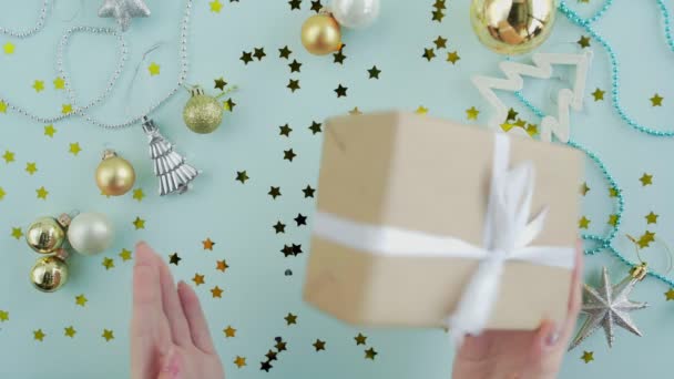 Donna scuote scatola regalo di Natale nelle mani della donna su sfondo blu vista dall'alto — Video Stock