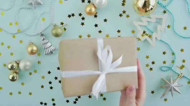 Mano femminile scuote scatola regalo di Natale nelle mani della donna su sfondo blu vista dall'alto — Video Stock