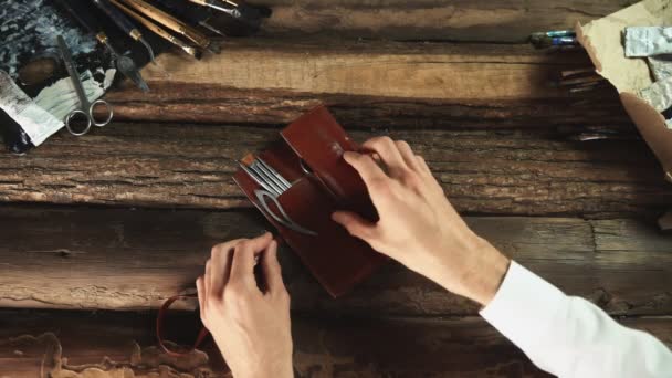 Мужчина-художник открывает кожаный чехол инструментами, кистями, мастихином — стоковое видео
