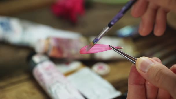 L'homme utilise un pinceau pour mettre de la peinture à l'huile de couleur rose sur petit pétale de fleur — Video