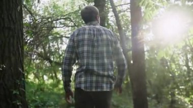 Kareli gömlekli adam güneşli bir günde parkta yürüyor..