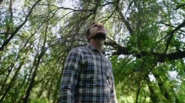 Ormanda dikilip etrafa bakınan yakışıklı beyaz bir adamın yakın çekimi. Günlük giysiler içinde sakin sakin bir günün tadını çıkaran bir adam..
