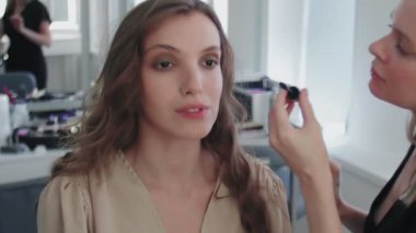 Stüdyoda oturan güzel ve genç bayan için Profesyonel Makyaj Süreci. Makyaj sanatçısı, maskarayı modele uygular