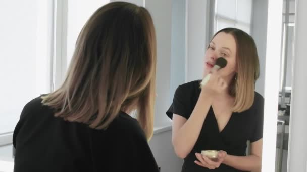 Επαγγελματική νεαρή γυναίκα κάνει ρουζ στο πρόσωπό της χρησιμοποιώντας πινέλο μακιγιάζ. — Αρχείο Βίντεο
