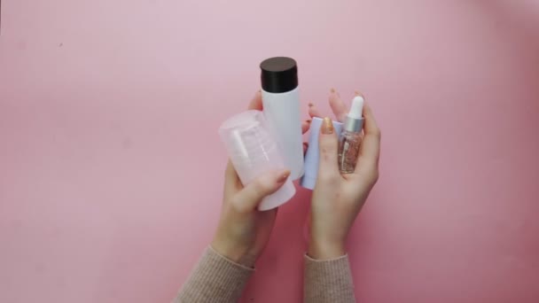 Wanita memegang botol plastik dengan kosmetik pada latar belakang merah muda — Stok Video