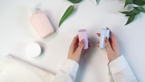 La mujer sostiene dos desodorantes azules y rosados en las manos. Tema de belleza plana disposición creativa laico con el entorno profesional. — Vídeos de Stock
