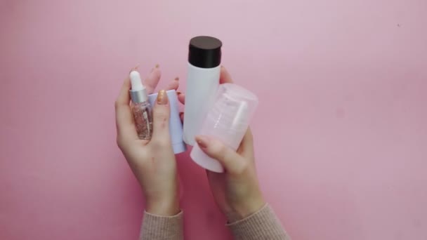 Mulher segura garrafa de plástico com cosméticos em fundo rosa — Vídeo de Stock