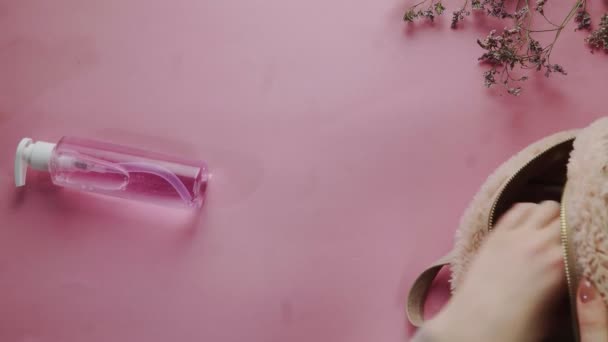 Vista superior de la mujer desempaca toda su cosmética de la bolsa sobre fondo rosa — Vídeos de Stock