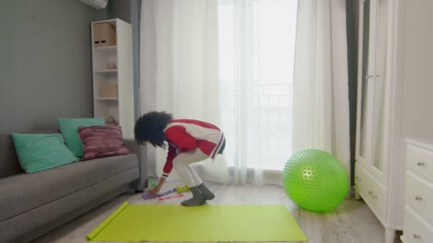 Ung, afroamerikansk kvinne hippie i fargerik sportstøy med krøllete afrohår gjør seg klar til å trene hjemme – stockvideo