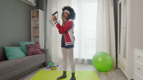 Young african american woman hippy in colourful sportswear with curly afro hairs is looking at the mirror after training — Stock Video