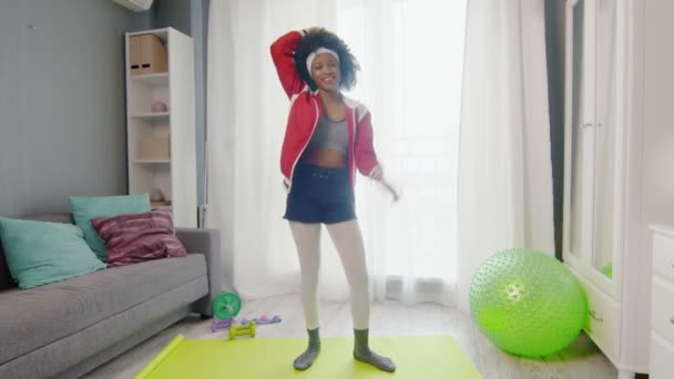 Young african american woman hippy in colourful sportswear with curly afro hairs looks at the camera and dances — Stock Video