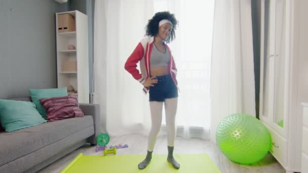 Fiatal vicces afro-amerikai nő hippi színes sportruházat göndör afro haj néz a kamera és a táncok — Stock videók