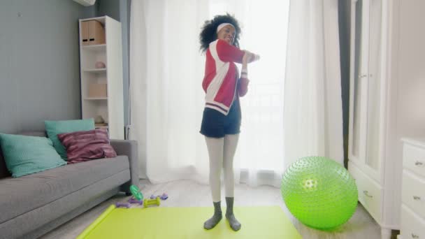 Young happy african american woman hippy in colourful sportswear with curly afro hairs looks at the camera and does stretch exercise — Stock Video