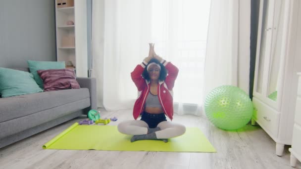 Young african american woman hippy in colourful sportswear with curly afro hairs sits in lotus pose and meditations — Stock Video