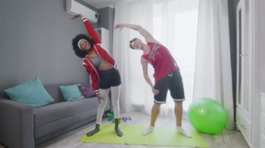 Neşeli beyaz adam ve Afrikalı Amerikalı kadın eski moda modeller odada dikilirken kaslarını esnetiyorlar.