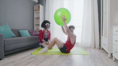 Kafkas erkek ve afro kadının evde iş yaptığı komik bir retro tarzı. Karın kasları egzersizi yapan komik bir adam. Evde spor topuyla antrenman yapıyor. Eşiyle, spor mizahıyla..