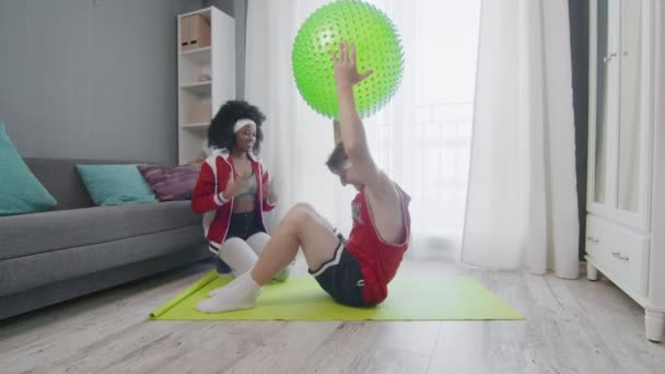 Funny retro style couple of Caucasian man and afro woman doing work up at home. Funny man doing abs exercises crunches at home with wife, fitness humor. — Stock Video