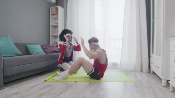 Funny retro style couple of Caucasian man and afro woman doing work up at home. Funny man doing abs exercises crunches at home with wife, fitness humor. — Stock Video
