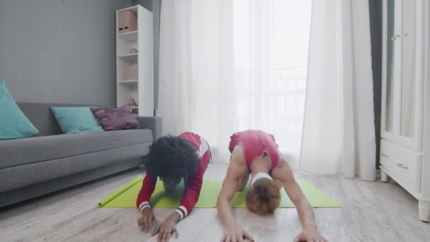 Divertido retro estilo pareja de caucásico hombre y afro mujer haciendo childs yoga pose en casa — Vídeos de Stock