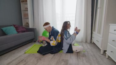 Komik erkek ve kadın spora yeni katılanlar renkli spor kıyafetleriyle elastik bantla el egzersizi yapıyorlar.