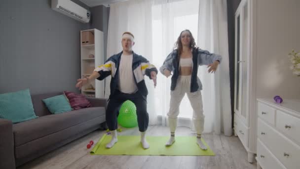 Lucu pasangan muda yang sehat pria dan wanita bekerja di rumah. Mereka melakukan latihan squat — Stok Video