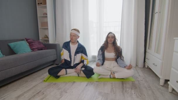 Keluarga muda fit duduk di lantai, bermeditasi bersama-sama, menjaga gaya hidup sehat. Pria itu menggunakan telepon saat pacarnya bermeditasi — Stok Video