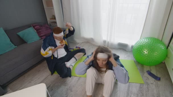 Pemuda bergaya retro makan pizza sementara pacarnya melakukan latihan perut — Stok Video