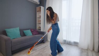 Mutlu ve neşeli genç bayan yerleri paspasla temizliyor ve telefonda konuşuyor.