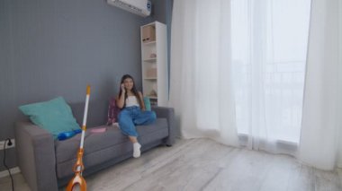 Evi temizledikten sonra yorgun genç bir kadın tek başına vagona oturuyor ve telefon kullanıyor.