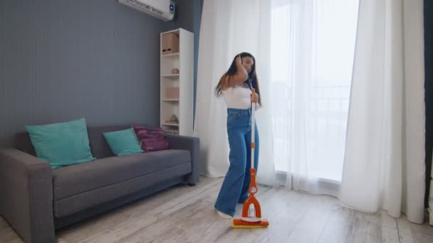 Молодая позитивная кавказка забавно танцует во время уборки дома — стоковое видео