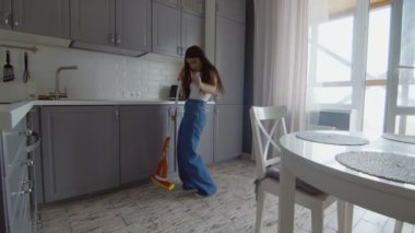Mutlu ve neşeli genç bir kadın yerleri paspas ve dansla temizliyor.