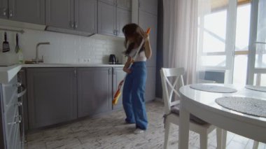 Mutlu ve neşeli genç kadın yerleri temizler ve gitar gibi paspasla dans eder.