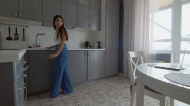 Serbest çalışan genç, modern bir kadın mutfaktaki dizüstü bilgisayarı kullanıyor. İşine odaklanmış bir kadın masada oturuyor ve evde çalışıyor..