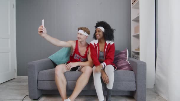 Pria kaukasia dan model gaya retro wanita afrika santai di sofa dan mengambil foto di telepon setelah sesi kerja — Stok Video