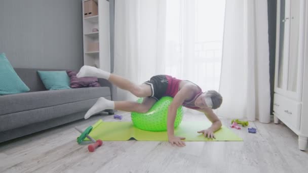 Retro joven con estilo hace ejercicios extraños y divertidos en una pelota de fitness en casa — Vídeos de Stock