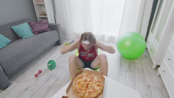 Aktiver, lustig aussehender Sportler, der auf dem Boden knirscht und versucht, eine frische, heiße Pizza auf den Tisch zu bekommen. Sportliche Aktivitäten zu Hause. — Stockvideo