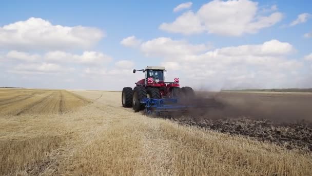 Un tractor roșu cu un plug invers plugulește un câmp . — Videoclip de stoc
