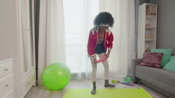 Young african american woman hippy in colourful sportswear with curly afro hairs does stretching exercises with elastic band on legs — Stock Video