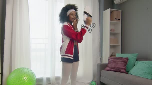 Jovem afro-americana hippy mulher em roupas esportivas coloridas com cabelos afro encaracolados está olhando para o espelho após o treinamento — Vídeo de Stock