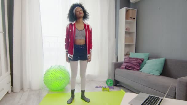 Young african american woman hippy in colourful sportswear with curly afro hairs is using a laptop for the workout. Workout the house online during the quarantine. — Stock Video