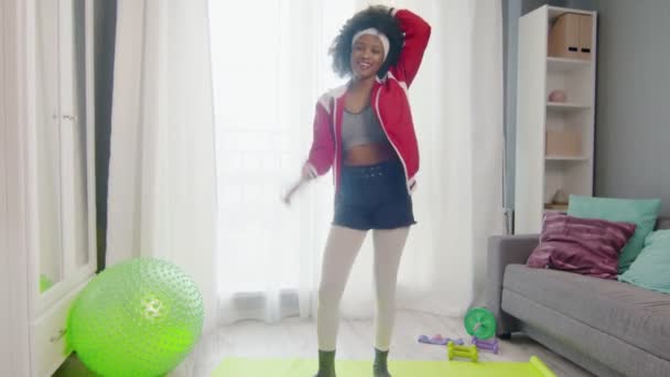 Young african american woman hippy in colourful sportswear with curly afro hairs looks at the camera and dances — Stock Video