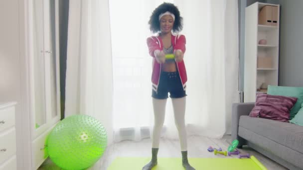 Young funny african american woman hippy in colourful sportswear with curly afro hairs looks at the camera and lifts green dumbel — Stock Video