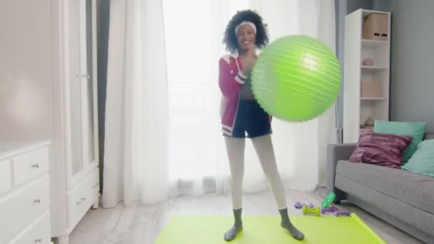 Giovane donna afro americana divertente hippy in abbigliamento sportivo colorato con capelli ricci afro guarda la fotocamera e tiene palla fitness in mano — Video Stock