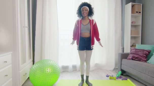 Young happy african american woman hippy in colourful sportswear with curly afro hairs looks at the camera and does warm up exercise — Stock Video
